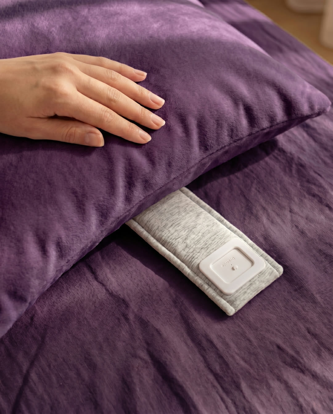 A Drowsie speaker tucked under the edge of a pillow on a deep-purple bed — only the person on that side can hear it.